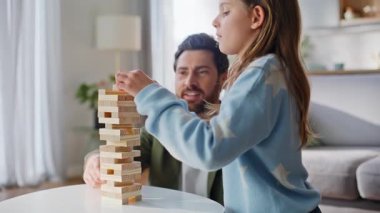 Baba kızı Jenga Modern Apartman Salonu 'nda oynuyor. Gülümseyen sakallı, sevimli genç kız ağaç bloklar inşa ediyor ve ailecek vakit geçiriyorlar. Neşeli aile aktiviteleri.