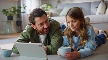 Gülümseyen baba kızı tablet izleyip oturma odasında yere uzanmış çay içiyor. Neşeli sakallı baba kahveyi yudumluyor çizgi filmlerin keyfini çıkarıyor bilgisayarın başında sevimli genç kızla ailecek vakit geçiriyor..