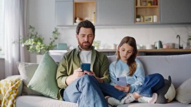 Akıllı telefonlara karışan baba kız rahat koltukta oturuyor. Kaygısız baba cep telefonu kızını online içeriği tartışırken gösteriyor. Mutlu bir aile, evdeki koltukta cep telefonu izliyor..