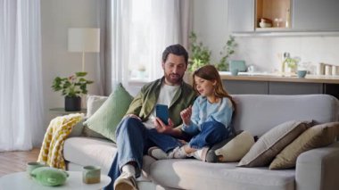 Çocuk bakıcısı cep telefonuyla video görüşmesine başlıyor rahat koltukta oturuyor. Rahat baba kız oturma odasında cep telefonu uygulaması kullanarak sanal görüşme yapıyor. Uzak ağ sohbeti
