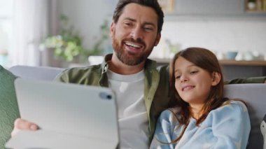 Gülümseyen çocuk çizgi filmlerin keyfini çıkarıyor dijital tablet rahat bir daire kanepesinde oturuyor. Mutlu baba kız gülerek evde bilgisayar seyrediyor. Rahat aile eğlencesi..