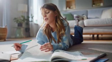 Genç kız apartman dairesinde ev ödevleriyle meşgul. Yakın plan. Okul derslerini okuyan, elinde kalemle evde tek başına yatan ciddi bir genç bayan. Sınav için modern daire okuyan tatlı bir kız öğrenci..