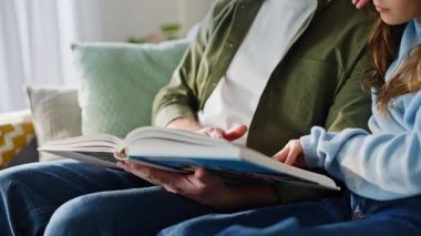 Gülümseyen adam kızını okuyor ve aile eğlencesini yakından yaşıyor. Mutlu sakallı baba sayfaları çeviriyor ve genç kız rahat koltukta oturuyor. Önemseyen baba okul kızına yardım ediyor. Ev eğitimi.