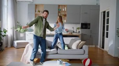 Eğlenceli baba kız hafif dairede dans ediyor. Neşeli sakallı baba, sevimli küçük kızıyla birlikte müzik çalıyor ve birlikte kanepeye atlayıp eğleniyorlar. Mutlu baba-oğul şakalaşması..