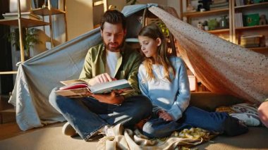 Sevgi dolu baba kitap okuyor meraklı kız battaniye kulübesinde güneşli bir oturma odasında oturuyor. Mutlu sakallı baba hikayeleri anlatan sayfalarca genç kızla bağ kurmanın tadını çıkar. Aile sevgi bakımı.