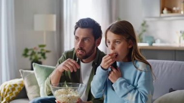 Gergin erkek kız, korku patlamış mısır yerken modern oturma odasının kapanışının keyfini çıkarıyor. Genç baba genç kız kanepede zıplayıp TV geriliminden korktu. Yerel televizyon görüntüleme