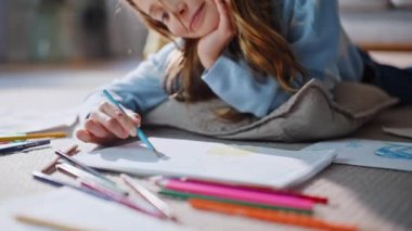 Kız eller, yaratıcı süreçten esinlenerek ev oturma odasını kapatarak resim çiziyor. Küçük mutlu liseli kız, yerde yatan kağıtları çizerken gülümsüyor. Yetenekli çocuk sanat hobisinin tadını çıkarıyor..