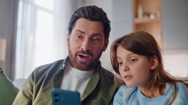 Babacık konuşuyor, el sallayan cep telefonu web kameralı daire kanepesi kapanışı. Mutlu baba, küçük kız internetteki toplantıyı karşılıyor. Uzak internet iletişimi kanepesinin keyfini çıkarıyor..