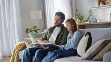 Sevgi dolu baba, küçük kızın rahat bir kanepede oturmasını açıklıyor. Önemseyen baba, mesaj okumaya meraklı küçük kız, ev ödevlerini destekliyor, konuyu kanepede öğreniyor..