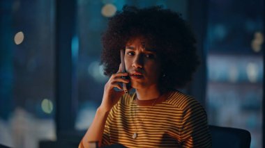 Stressed businesswoman speaking smartphone at evening corporate workspace closeup. Worried african american woman discuss problem by phone. Concerned overtime manager calling cellphone in night office