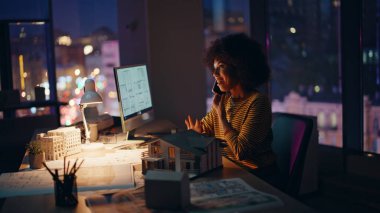 Mimari tasarımcı gece geç saatlerde ofis gayrimenkul şirketinden arıyor. Gülümseyen Afro-Amerikan kadın bina tasarımını telefonla tartışıyor. Gece işyerinde konuşan mutlu mimar..
