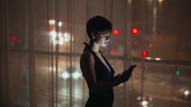 Cep telefonu panoramik pencere odasını kullanan akşam kadını. Hayalperest, rahat bir bayan lüks bir dairede cep telefonu ihbarı alıyor. Muhteşem üzgün model, gece manzaralı erkek arkadaş bekliyor.