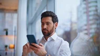 Kapalı çekim gülümseyen adam akıllı telefon mesajı atıyor e-postalar açıyor panoramik pencere. Mutlu yöneticiler ara verip sosyal medyadan keyif alıyorlar. Orta yaşlı sakallı işadamı tek başına dinleniyor.