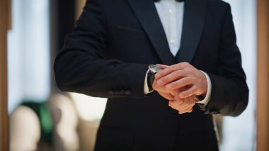 Yakından bakan adam, kostüm odasını kullanarak saati kontrol ediyor. Sakallı resmi takım elbiseli beyefendi, yansıyan yansıma yıldönümü partisini tek başına hazırlıyor. Yakışıklı, bakımlı bir iş adamı. İçerideki aynaya bakıyor.