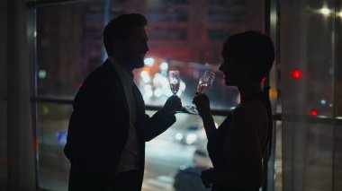 Akşam eşleri siluet özel konuşma yakın çekim. Karanlıkta büyük bir dairede duran gevşemiş gözlük. Erkek kadın aşıklar romantik yakınlaşmalar yaşıyorlar.