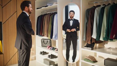 Resmi takım elbiseli adam memnun. Aynadaki yansımayı işaret ediyor. Ceketinin düğmelerini ilikleyen kendine güvenen zarif bir beyefendi. Sakallı, gülümseyen iş adamı parti için hazırlanıyor.