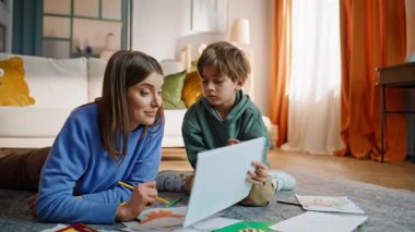 Küçük oğlu, sevgili annesini gösteriyor. Yerde yatıyor, yakın plan. Pastel boyalarla resim çizen yakışıklı yaratıcı çocuk sanat hobisinden hoşlanıyor. Mutlu anne albümü arıyor. Hayal gücü için çocuğu övüyor..