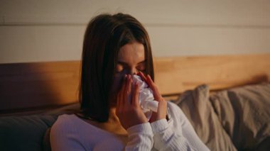 Elinde peçeteyle sümküren bir kadın yatağında rahat bir şekilde yatıyordu. Başa dokunan üzgün kadın baş ağrısı çekiyor. Sıcaklık ölçer gibi görünüyor. Grip virüsü konsepti.