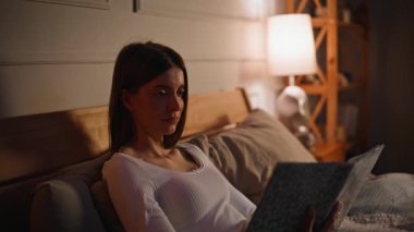Rahat kadın kitap okuyor. Rahat yatak odalarında uzanıyor. Yatak odasını kapatıyor. Edebiyat hobisinin keyfini çıkaran sakin, rahat bir yatak aydınlatmalı, yumuşak bir lamba. Uyku zamanı rutini.