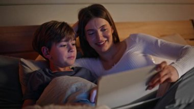 Gülümseyen kadın, oğlunun sıcak bir yatak odasında tableti karıştırırken yalan söylüyor. Mutlu genç anne, masal evi bilgisayarında rahat bir yatak uzanıyor. Sevimli küçük çocuk içeride annesiyle konuşuyor.