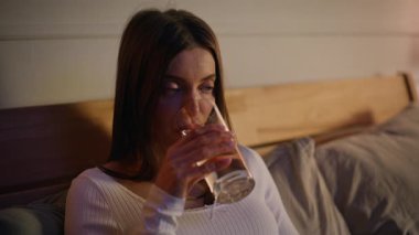 Yakından su içen kadın yumuşak lamba ışığında rahat bir yatak odasında yatıyor. Gülümseyen esmer, taze içeceğini yudumluyor, sıcaklığı ölçüyor, termometreye bakıyor, rahat bir evde yatıyordu. Ev iyileştirme kavramı