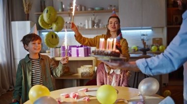 Aile sürprizi doğum günü kızı şirin pastayı yakın plan getiriyor. Şaşırtıcı mutlu çocuk mum üflüyor, kutlama için alkışlıyor. Gülümseyen genç aile kardeş heyecanlı çocuğu kutluyor.