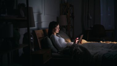 Tablete dokunan, parlayan tablete dokunan ev hanımı gece yarısı rahat yatağında uzanıyor. Gülümseyen genç esmer iş kadını uyumadan önce e-posta bilgisayarı okuyor. İnternet alışverişi yapan rahat bir bayan..