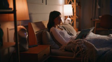 Huzurlu bayan, kitapların keyfini çıkarın. Kapalı, karanlık yatak odası örtüsü. Rahat genç bayan uyumadan önce edebiyat okuyor. Sakin çekici esmer, ilginç bir roman, rahatlatıcı bir gece yatağı içeriyor.