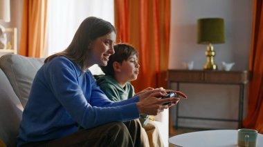Anne oğul video oyunu oynuyor modern apartman kanepede oturuyor. Rekabetçi genç kadın mutlu çocuk çevrimiçi zaferi kutluyor birlikte mutluluğu hissediyorlar. Neşeli aile evde oyun oynamayı sever.