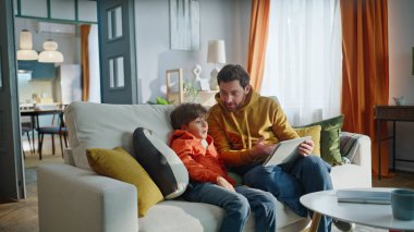 Baba oğul evde kanepede oturup tablet oynuyor. Yakın plan. Gülümseyen bekar baba, küçük çocuk hafta sonu internette komik içerik tartışması yapıyor. Ana çocuk tarama aygıtı.