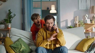 Oğul, babasının cep telefonunu aramasını engelliyor. Evdeki kanepeyi kapatıyor. Stresli sakallı adam akıllı telefondan konuşuyor. Küçük gürültücü çocuk kanepede koşuşturup bağırıyor. Babalık sorunu.