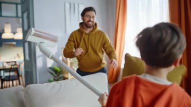 Neşeli baba, elinde elektrikli süpürge tutan neşeli oğlana yastık fırlatıyor. Aktif baba, küçük çocuk birlikte oynaşıp eğlenceli ev işleri yapıyor. Gülümseyen baba şirin çocuk oyunu.