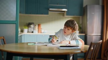 Akıllı okul çocuğu defter yazıyor. Ödevlerini yapıyor. Mutfak masasında oturuyor. Ciddi bir ilkokul öğrencisi, ev ödevi kitabında kafası karışmış bir şekilde çalışıyor. Çalışkan küçük çocuk, konuyu öğreniyor..