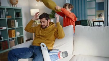 Sevimli oğul yastıklı sakallı babayla dövüşüyor. Oturma odasındaki kanepede oturuyor. Gülümseyen baba, aktif küçük çocukla oynarken aile aktivitelerinin keyfini çıkarıyor. Neşeli çocuk, sana iyi eğlenceler adamım..