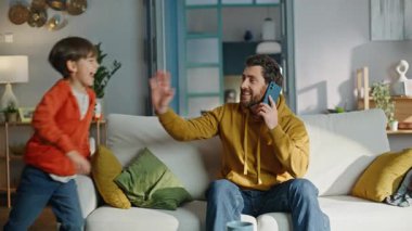 Çocuk, babayı koltukta otururken aramak dikkatini dağıtıyor. Stresli genç adamın cep telefonundan konuşması yaramaz küçük oğlanın evde kanepede yüksek sesle oynamasından rahatsız oldu. Gergin baba bağıran çocuğu sakinleştiriyor..