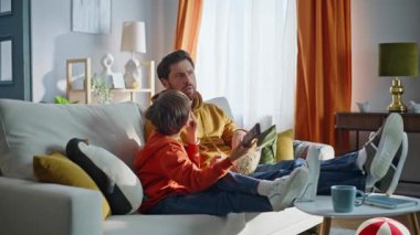 Baba oğul film seyrediyor oturma odasındaki kanepede birlikte oturuyorlar. Kaygısız baba, küçük çocuk televizyon izlemekten zevk alıyor. Gülümseyen ebeveyn çocuk abur cubur yiyor..