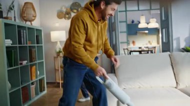 Gülümseyen baba halı süpürüyor modern oturma odasında sevimli aktif çocuğu oynuyor. Yastık fırlatan neşeli küçük çocuk sana mutlu sakallı baba. Komik oyuncu adam elektrikli süpürgeyle savaşıyor..