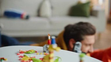 Mutlu baba, gülümseyen küçük çocukla oyun oynamaktan zevk alıyor. Oturma odası zeminine yakın çekim. Neşeli sakallı adam oyuncak kamera kullanarak sevimli çocuğun fotoğrafını çekiyor. Lego oynayan sevimli oğul aile hafta sonunu rahatlatıyor..