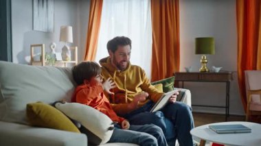 Baba çocuk videosu, konuşan tablet web kamerasını arıyor. Ev kanepede yan yana oturuyorlar. Gülümseyen baba, tatlı oğul internette el sallıyor, kanepede dinleniyor. Aile video arama platformu bilgisayarı.