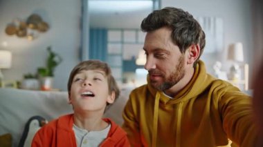 Pov videolu baba oğul oturma odasındaki kanepeyi görüntülüyor. Yakın çekim. Gülümseyen sakallı, tapılası çocuk internette el aleti kamerasıyla konuşuyor. Aile blogcuları