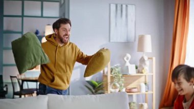 Mutlu baba, evde oyun oynayan küçük, aktif bir evlat. Gülümseyen sakallı adam oturma odasındaki sevimli çocuğa yastık fırlatıyor. Neşeli bekar baba çocuğu, birlikte eğleniyor..