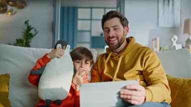 Baba oğul tableti arıyor. Kanepede yan yana oturuyorlar. Gülümseyen sakallı baba mutlu küçük çocuk sanal toplantıda konuşuyor ve web kameralı bilgisayara bakıyor. Aile video aramasından zevk alır