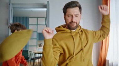 Erkek evlat evde dans edip enerjik müzik eşliğinde yakınlaşıyor. Komik sakallı baba tatlı çocuk aktif evde oyun zamanının tadını çıkarıyor. Gülümseyen baba, çocuk kanepeden atlayarak eğleniyor. Çocukluk eğlencesi.