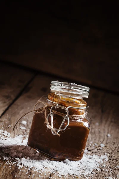 Caramello salato fatto in casa in un barattolo di vetro con coperchio, sale spruzzato — Foto Stock