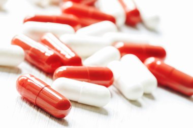 Red and white tablets in capsules on a white wooden background clipart