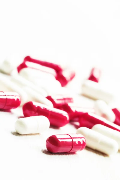 Красно-белые таблетки в капсулах на белом деревянном фоне — стоковое фото