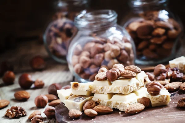 Delicious white chocolate, almonds, hazelnuts, on the old wooden background — Stock Photo, Image