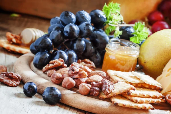 Snack tallrik: vindruvor, päron, hasselnötter, mandlar, valnötter, ost Maasdam och honung — Stockfoto