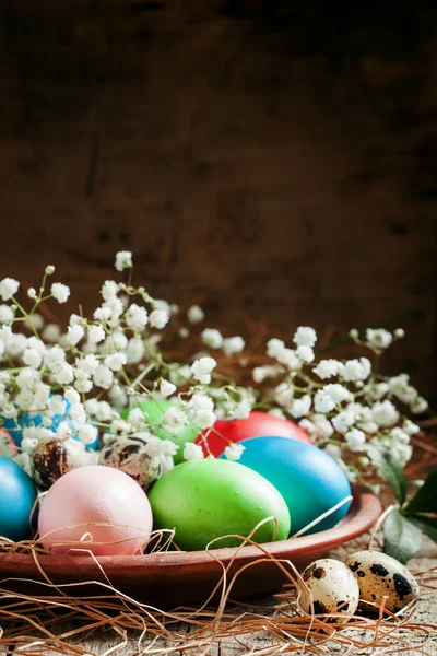 Многоцветные пасхальные яйца и перепелиные яйца на глиняной тарелке — стоковое фото