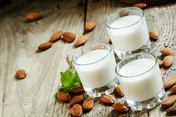 Almond milk in small glasses and spilled dry almonds — Stock Photo, Image